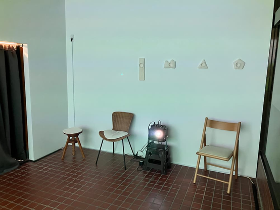 nobi の映像上映風景。写真は観客席側を写したもので、プロジェクターが映っているが投影面は見えていない。席が3席ある。また、壁には作品が展示されている。