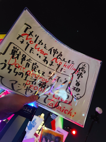 手書きのプラカードの写真。「高市首相、アメリカと仲良しになりたいあまりに戦争肯定して笑ったりうちらの生活破壊するのマジやめて」と書いてある。